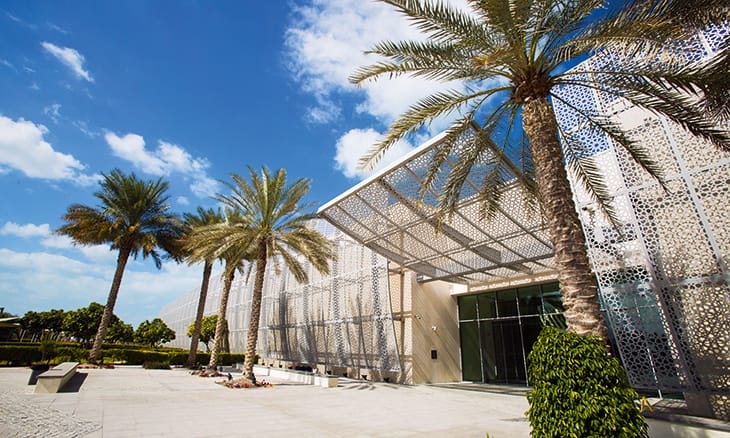 Modern building with a perforated metal facade, palm trees, and a clear blue sky in the background.