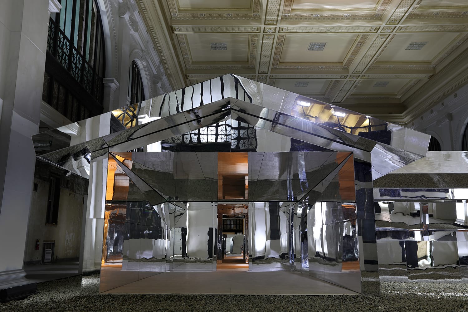 Reflective architectural installation in a grand hall with ornate ceiling, showcasing modern design and lighting contrasts.