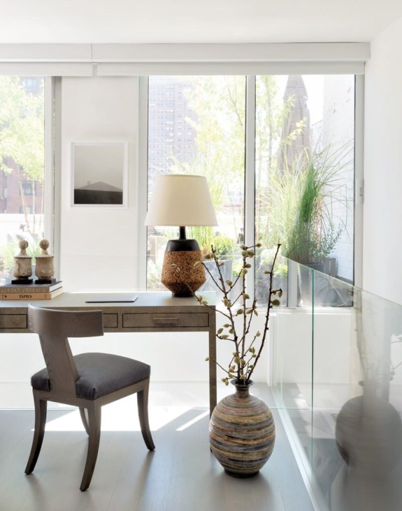 Modern home office with wooden desk, chair, vase, and large window overlooking outdoor greenery. Bright and inviting workspace.