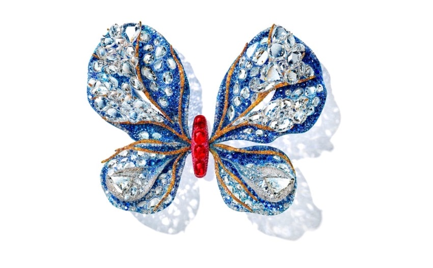 Blue and silver jeweled butterfly brooch with red accents on a white background.
