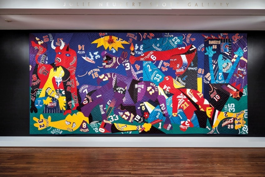 Colorful quilt art featuring numbers and sports jerseys in a vibrant collage, displayed in a gallery setting.