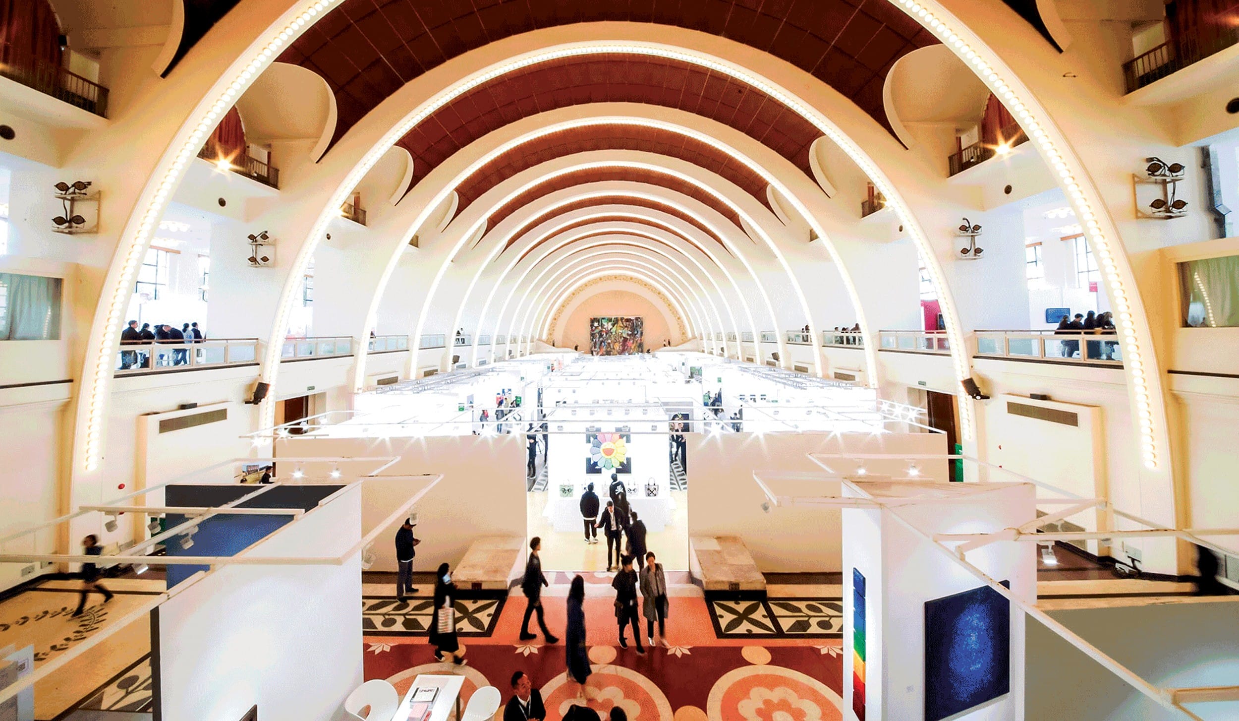 Wide-angle view of a spacious exhibition hall with unique architecture, arched ceiling, and people walking around.