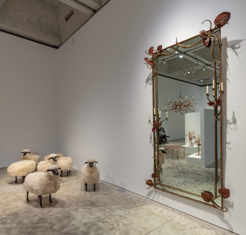 Several sheep sculptures facing an ornate mirror in an art gallery exhibit room.