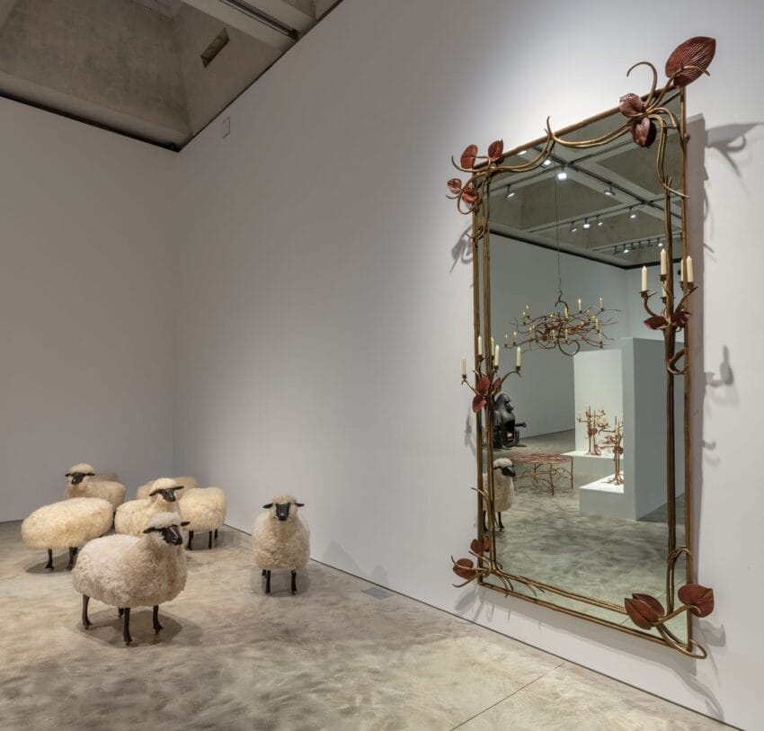 Several sheep sculptures facing an ornate mirror in an art gallery exhibit room.