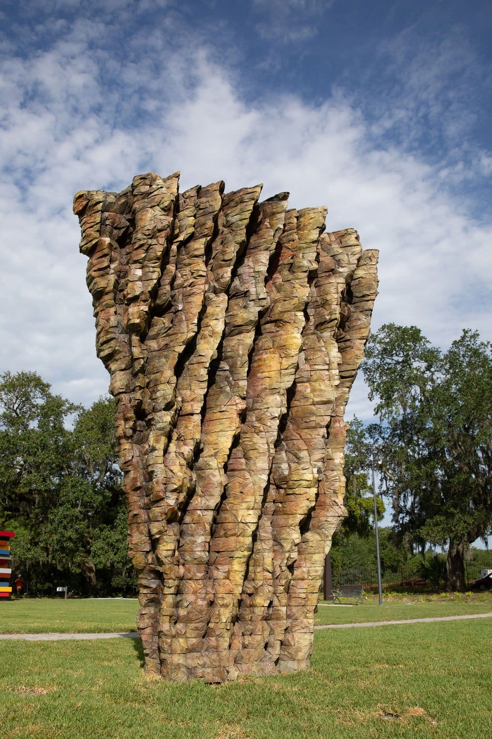 Large abstract stone sculpture in a park setting with trees and a partly cloudy sky in the background.