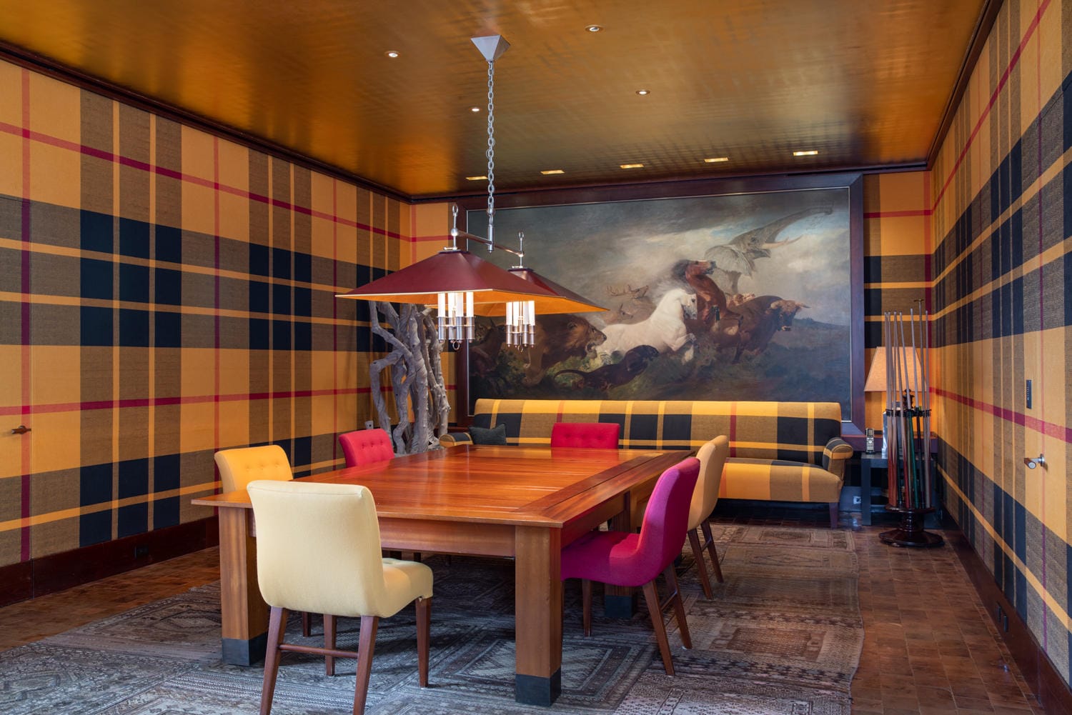 Dining room with plaid walls, colorful chairs around a wooden table, large mural, and modern chandelier.