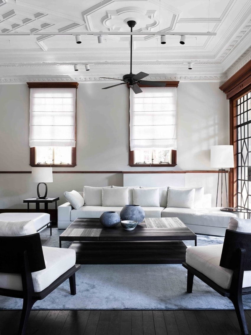 Elegant modern living room with white sofas, dark wooden coffee table, ceiling fan, and stylish decor elements.