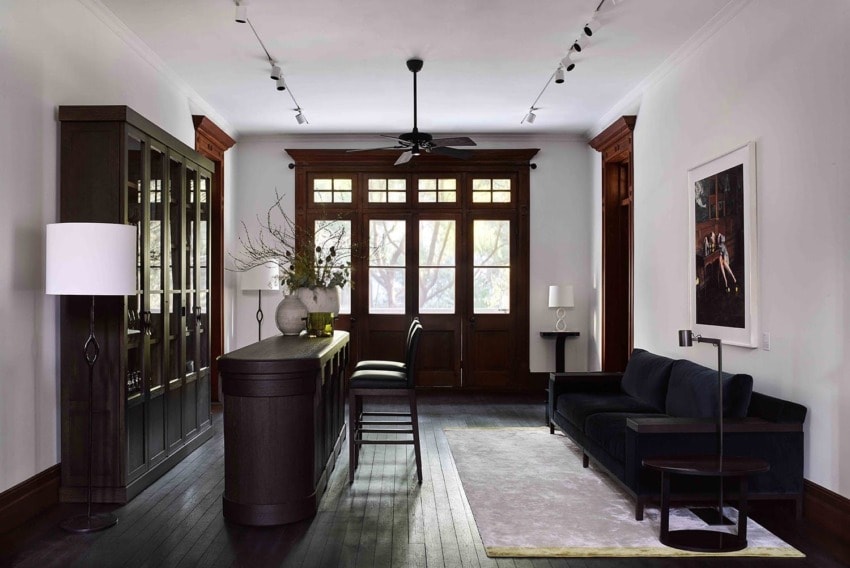 Modern living room with dark wood furniture, large windows, an elegant bar area, and a cozy black couch.