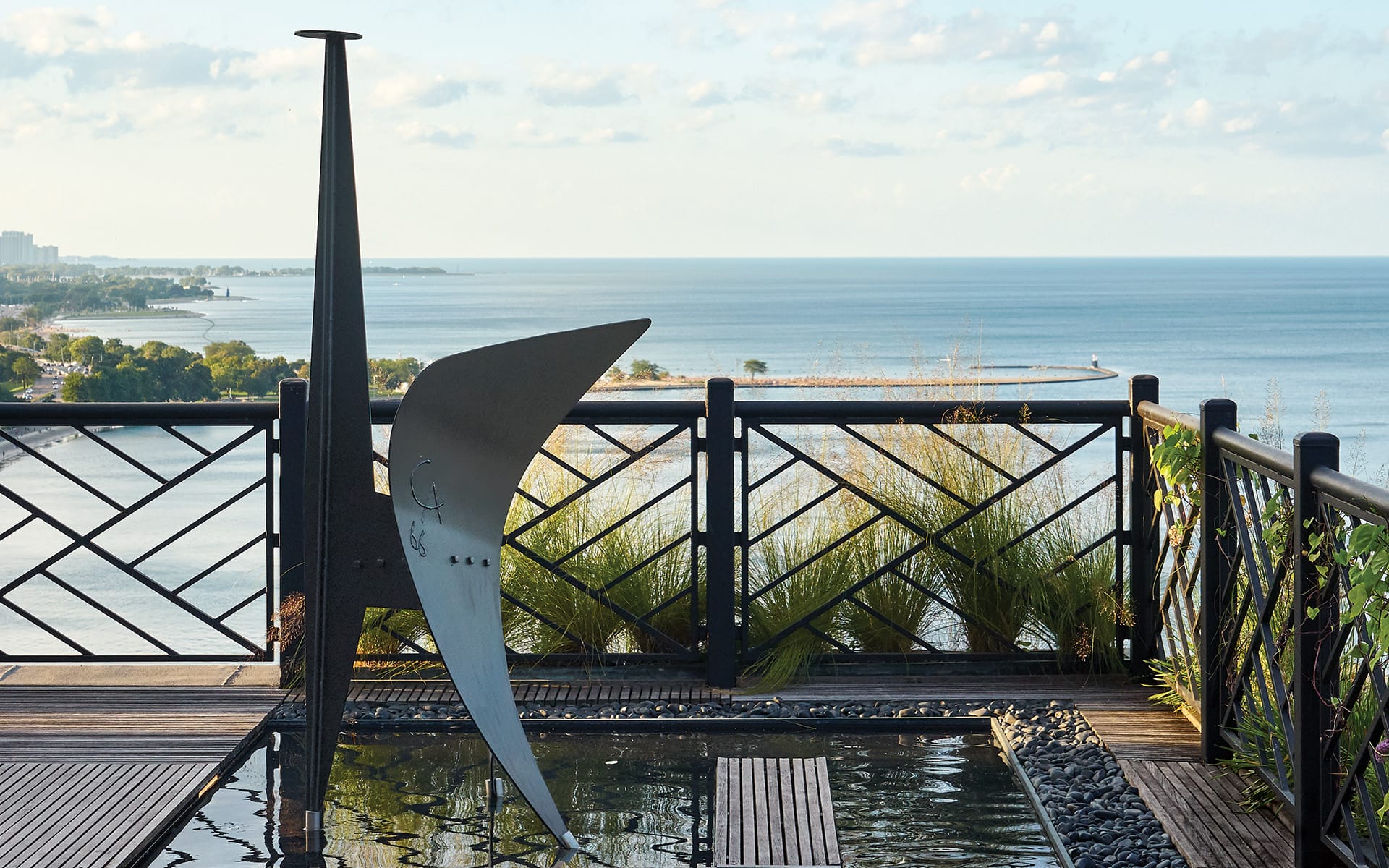 Rooftop terrace with modern sculpture, lush greenery, and ocean views under a partly cloudy sky.