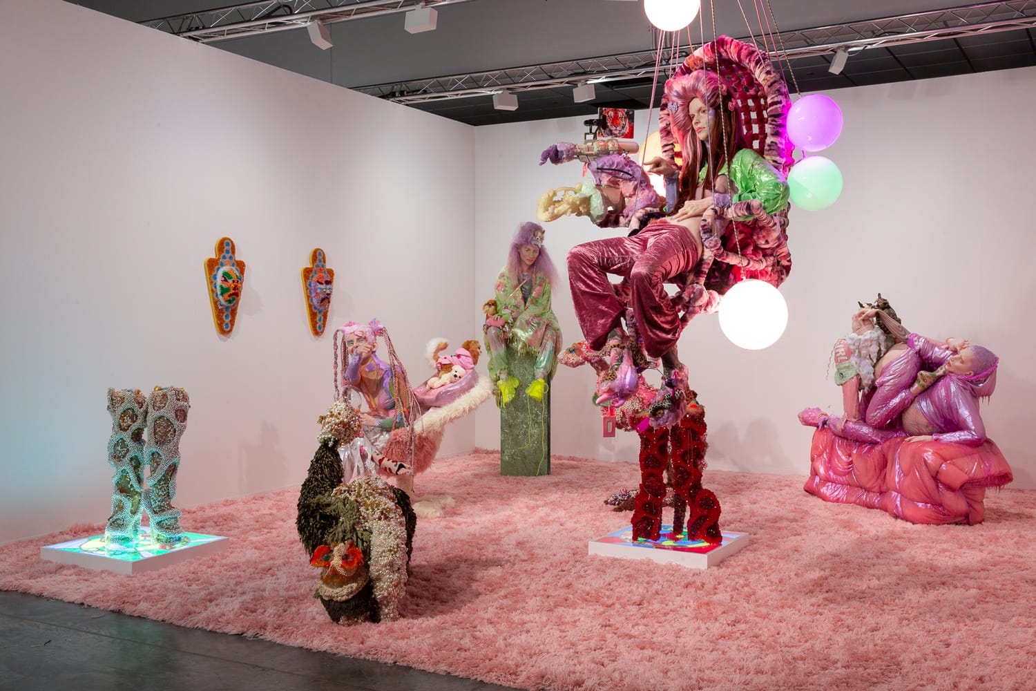 Colorful abstract art installation featuring people in vibrant costumes with textured, whimsical designs in a bright gallery setting.