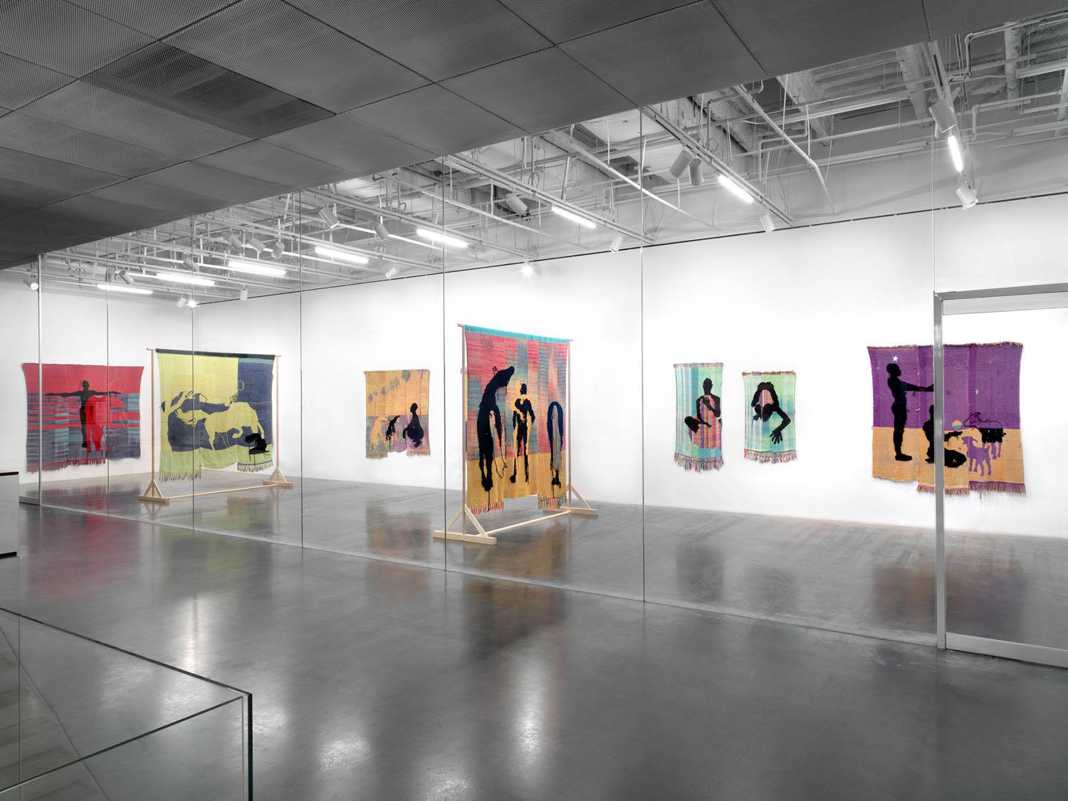 Art exhibition with colorful tapestries depicting silhouettes on gallery walls.