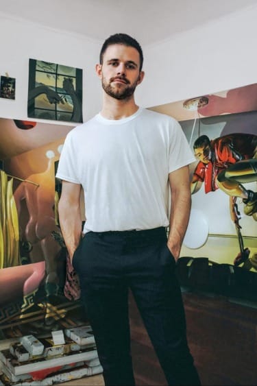 Man in a white t-shirt standing in front of colorful abstract art on a wall in a room.