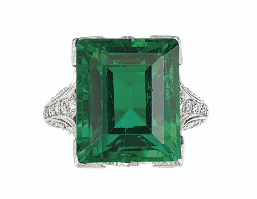 Emerald-cut green gemstone ring with intricate silver band detailing, on a white background.