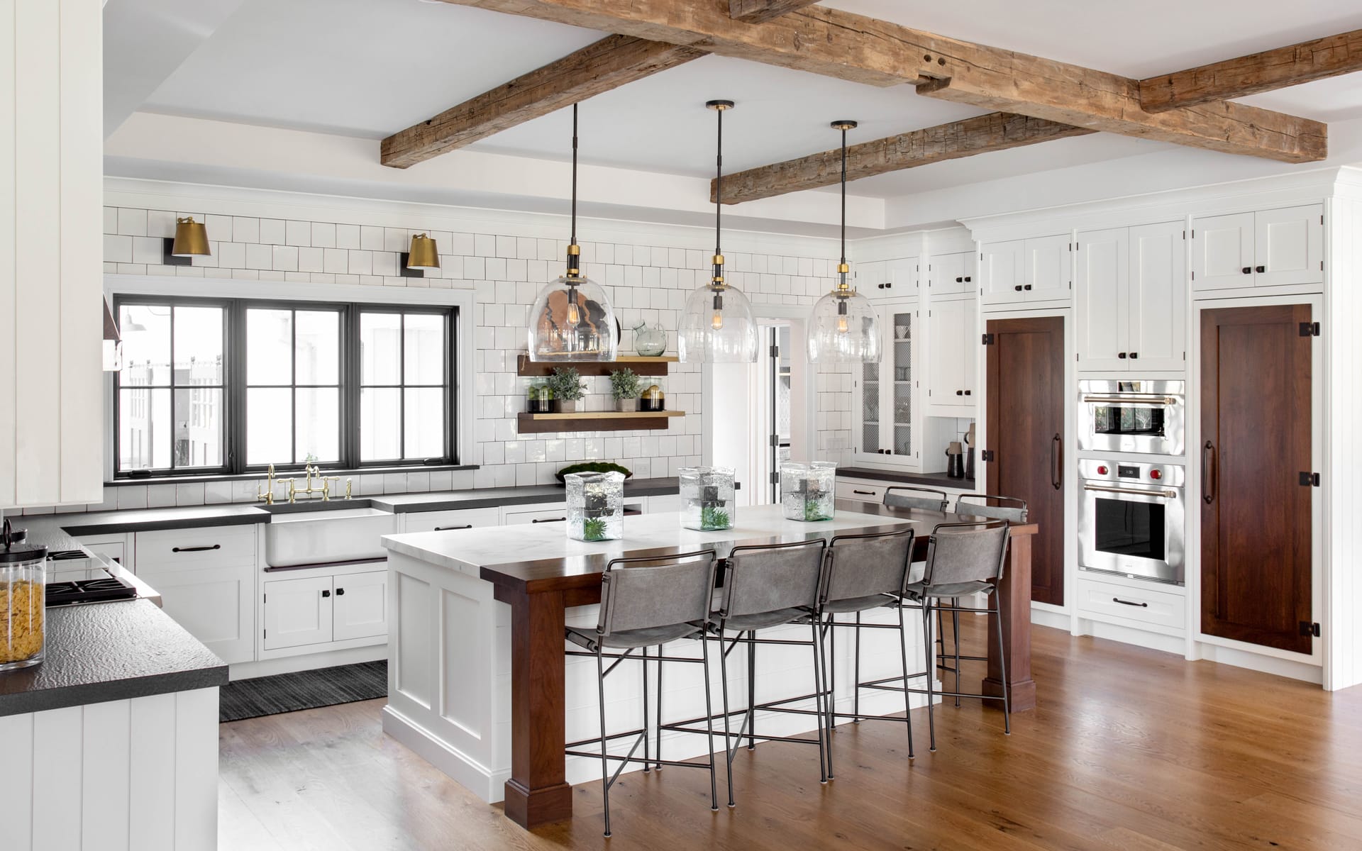 Modern kitchen with white cabinets, wood beams, and island with bar stools and pendant lights.