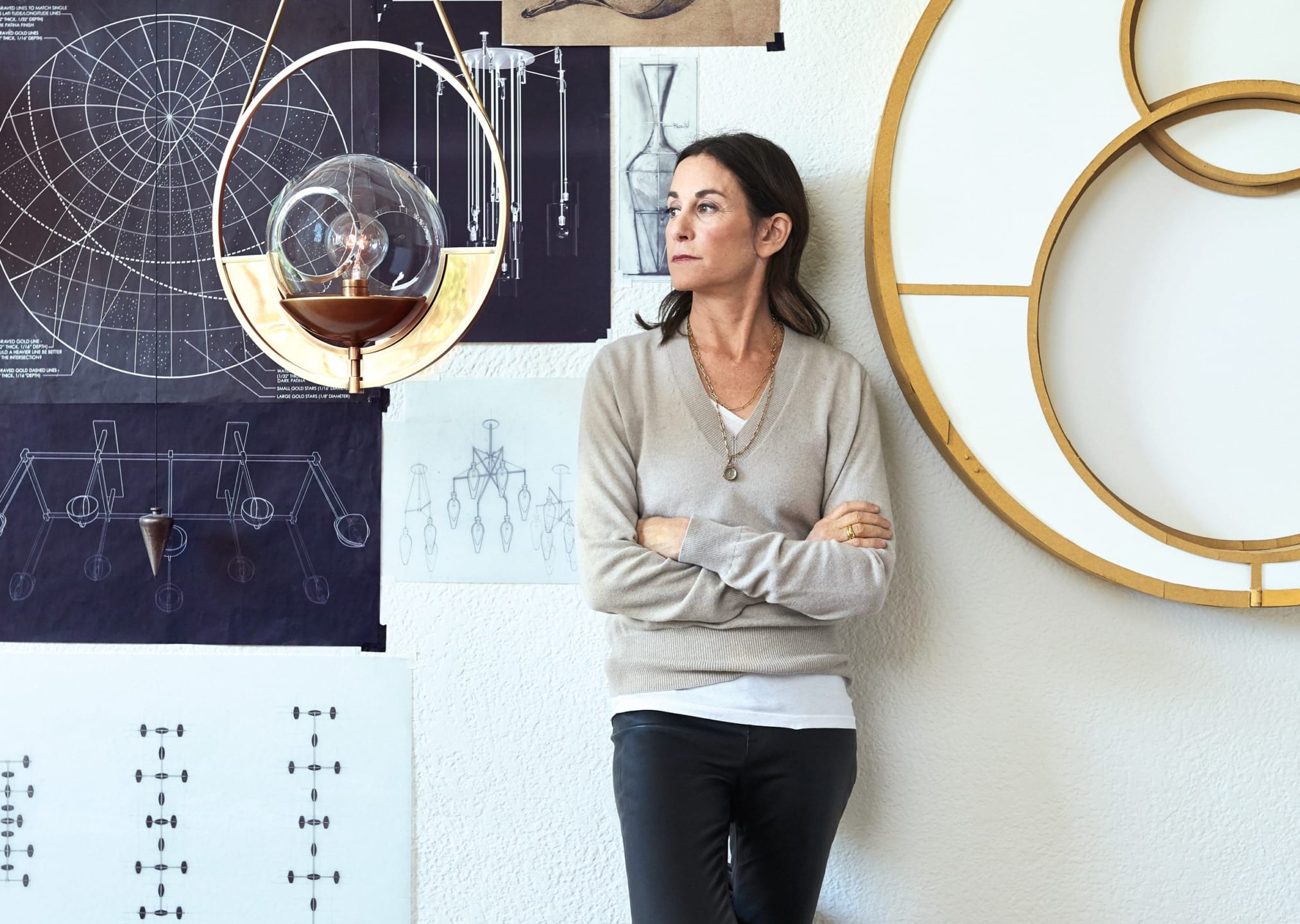 Woman leaning against a wall with design blueprints and diagrams behind her, looking away thoughtfully.