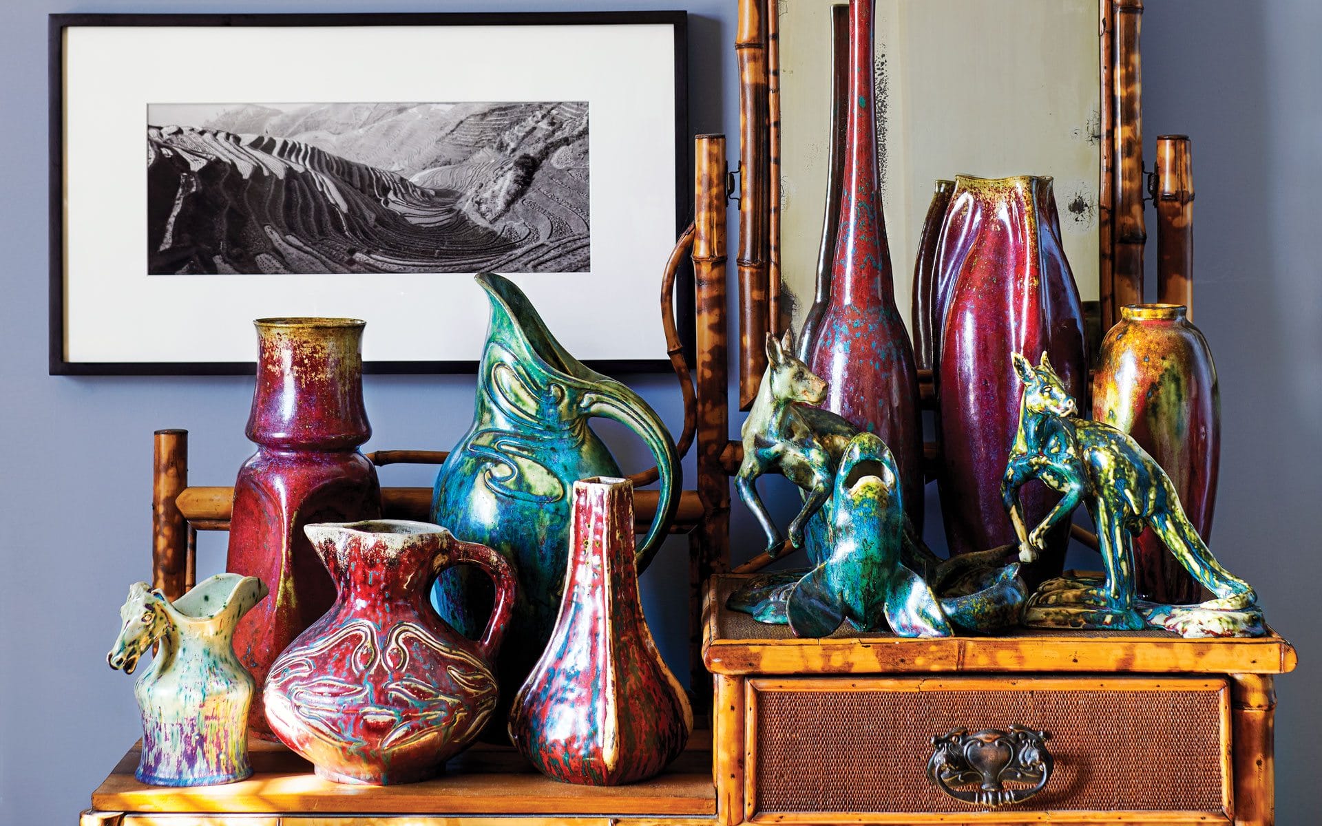 Colorful ceramic vases and horse figurines displayed on wooden dresser with framed black and white photograph in background.