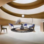 Modern spiral interior with a round table, blue chairs, a tall lamp, and a decorative plant on a rug.