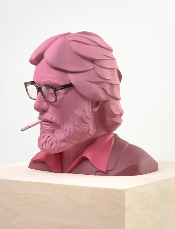 Pink sculpture of a bearded man with glasses and a lit cigarette, displayed on a wooden pedestal.
