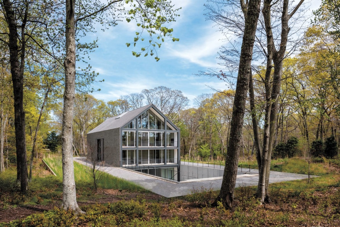 Modern glass house surrounded by trees in a woodland setting under a blue sky