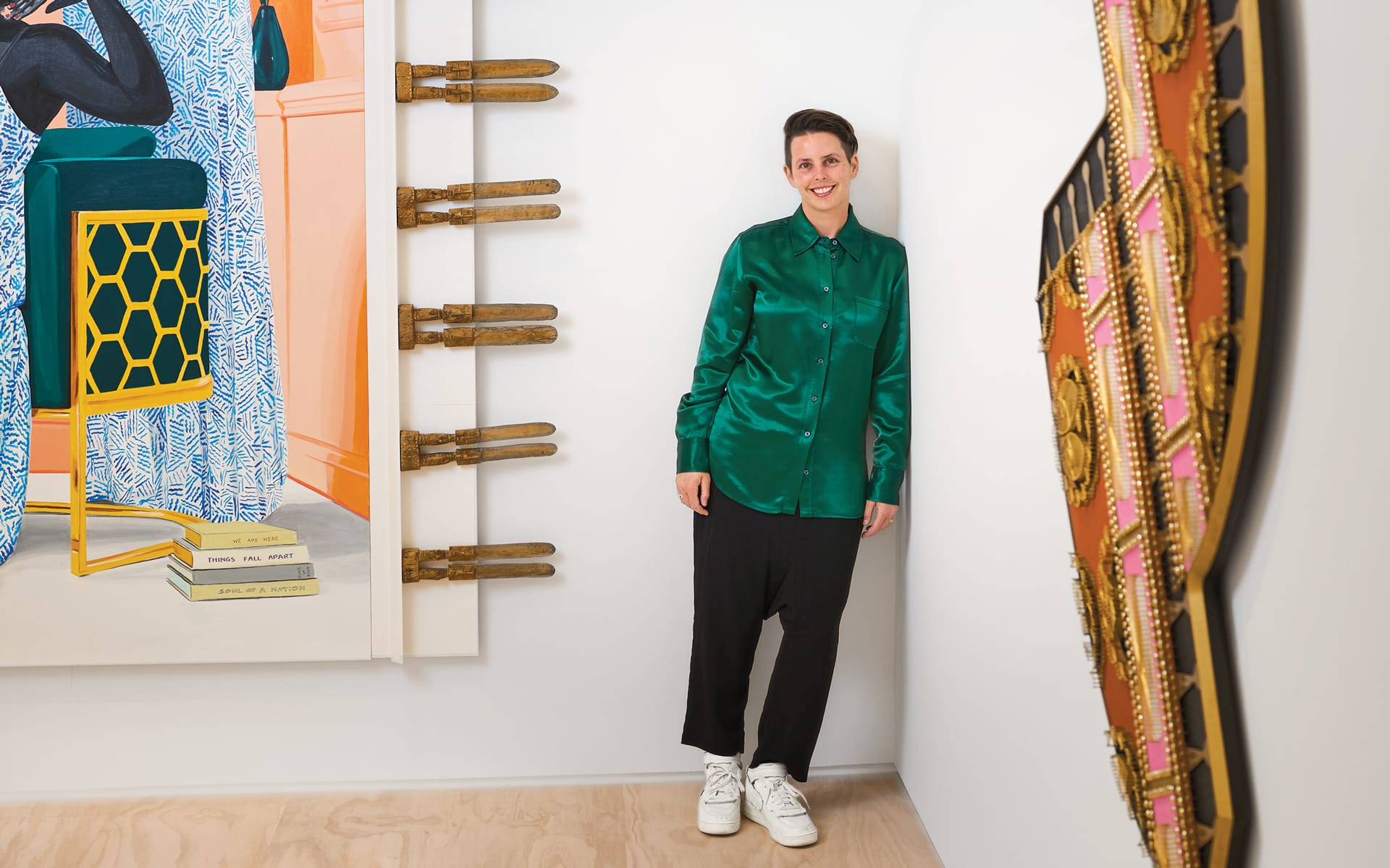 Person in green shirt leaning against a white gallery wall, surrounded by vibrant modern art pieces.