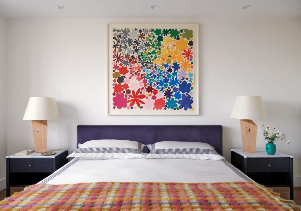 Bedroom with colorful floral wall art, two lamps on side tables, and a bed with a checkered blanket.