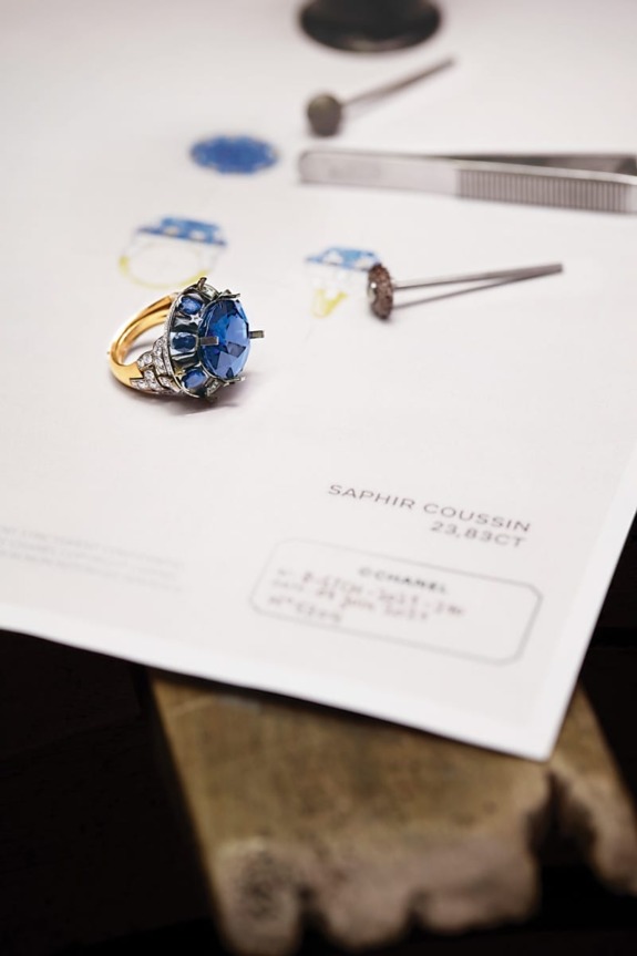 Blue sapphire ring with design sketch and jeweler's tools on a table.
