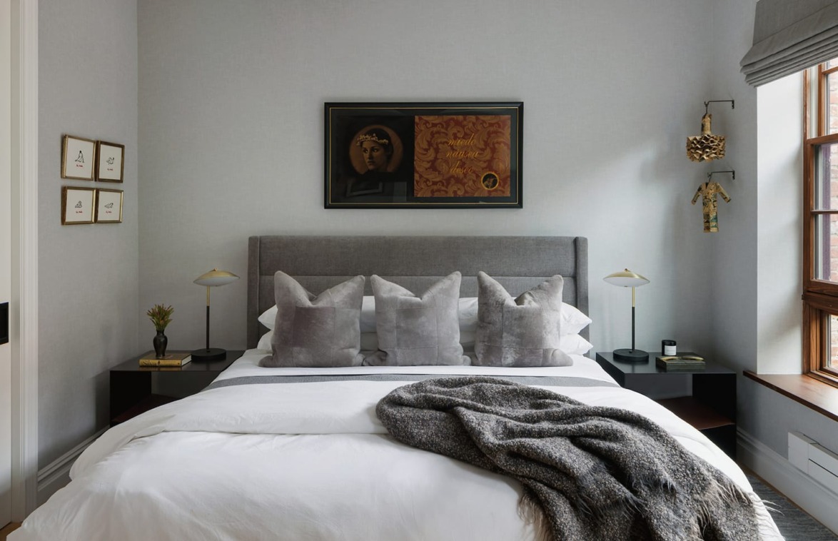 Modern bedroom with a gray upholstered bed, white bedding, decorative pillows, artwork above the headboard, and a cozy throw blanket.