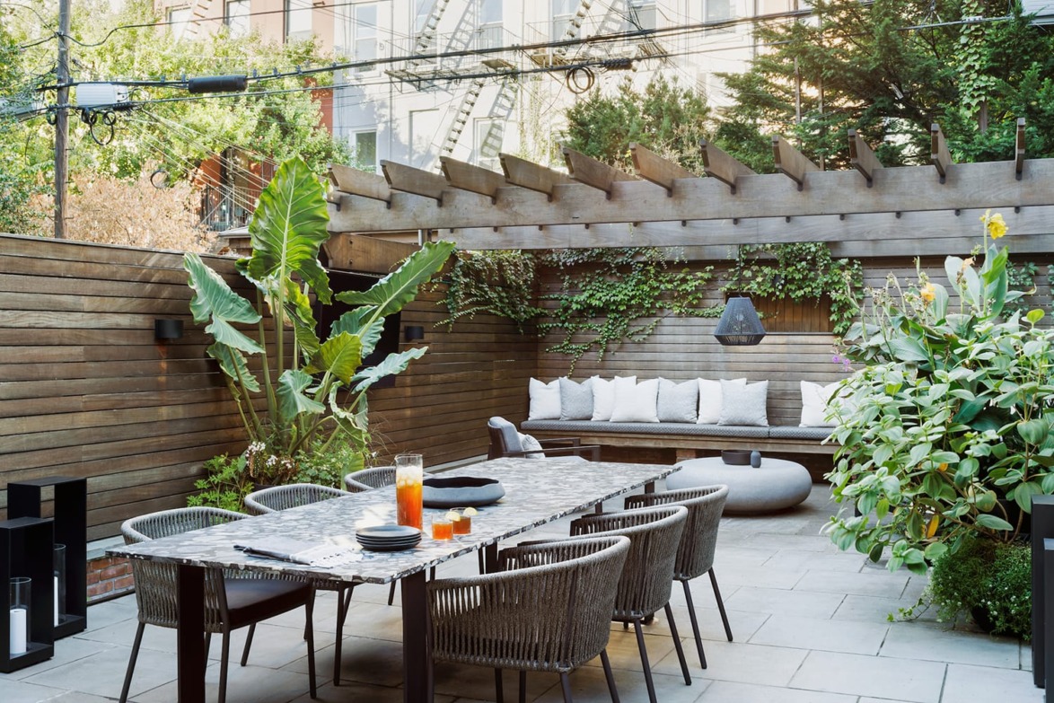 Modern patio with wooden pergola, outdoor dining table, and lush greenery in a serene backyard setting.