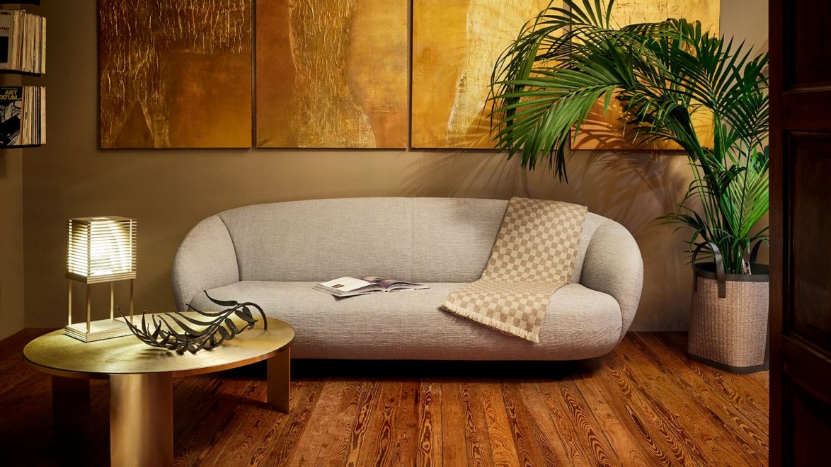 Modern living room with a gray sofa, wooden coffee table, lamp, plant, and abstract gold paintings on the wall.
