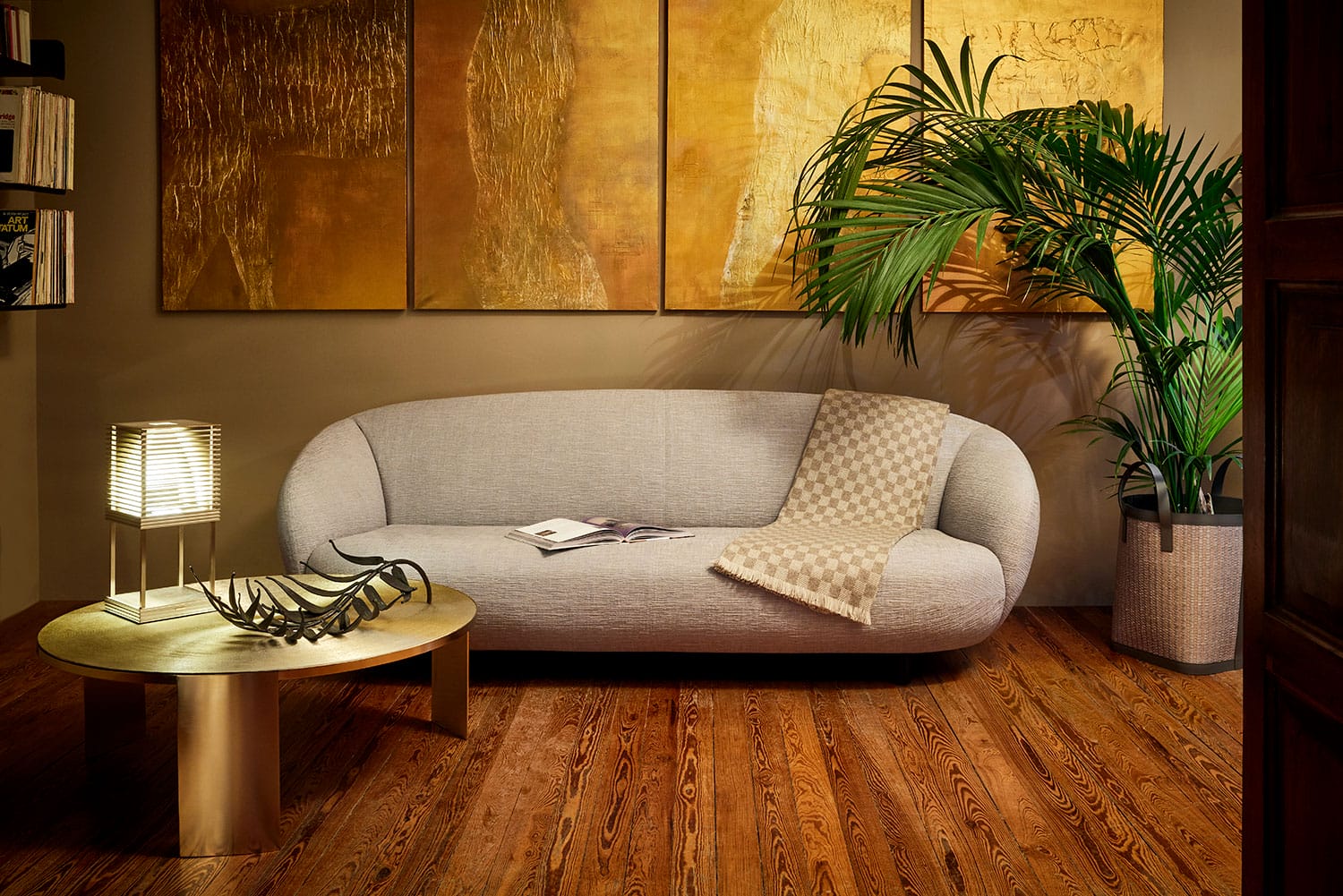 Modern living room with a gray sofa, wooden coffee table, lamp, plant, and abstract gold paintings on the wall.
