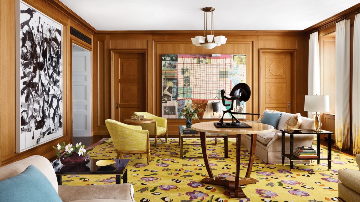 Modern living room with colorful art, wooden walls, yellow patterned rug, and various elegant furniture pieces.