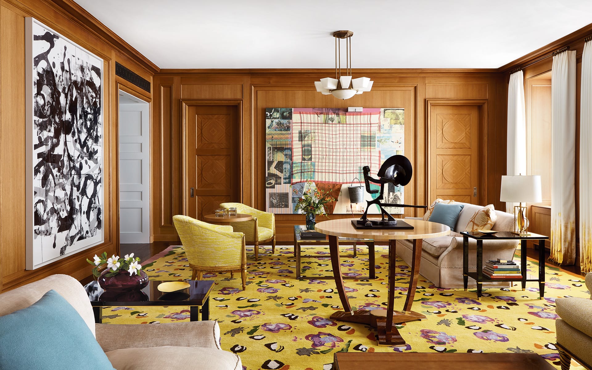 Modern living room with colorful art, wooden walls, yellow patterned rug, and various elegant furniture pieces.