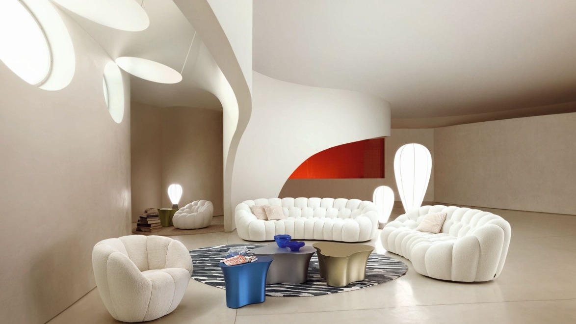 Modern living room with white tufted sofas, abstract lighting, curved walls, and a round rug with coffee tables.