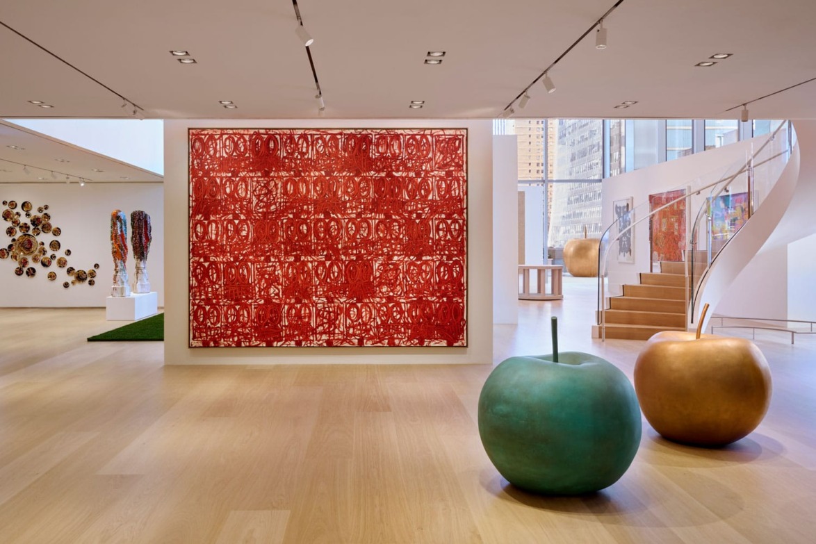 Modern art gallery with colorful sculptures, a large red abstract painting, and spiral staircase in a spacious, well-lit room.
