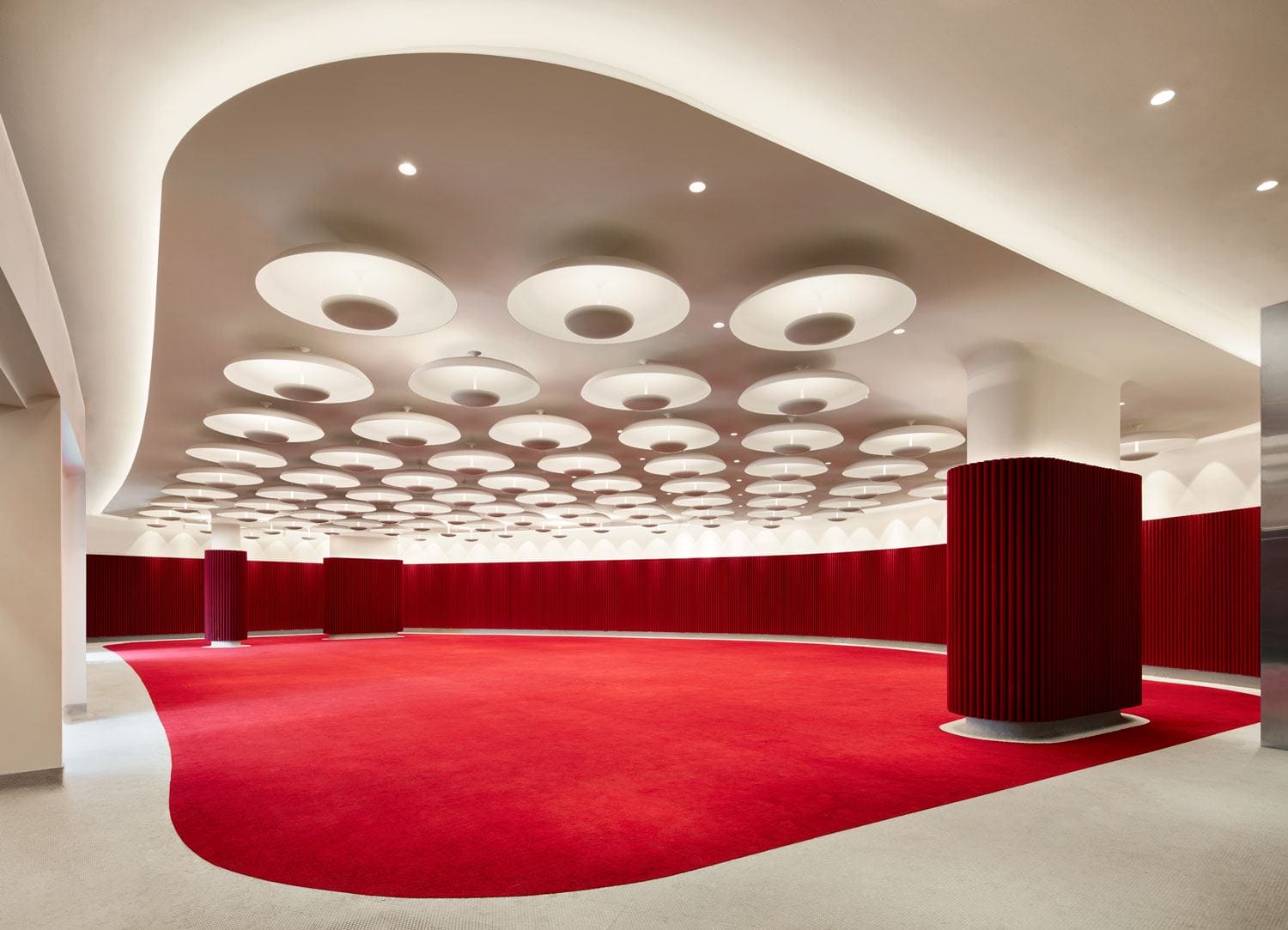 Modern interior with circular ceiling lights and red carpet, featuring curved red walls and pillars.