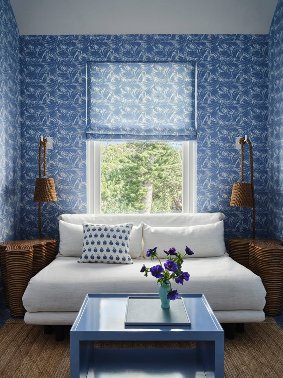 Cozy blue-themed living room with patterned wallpaper, white sofa, decorative pillows, and a vase of flowers on a blue table.