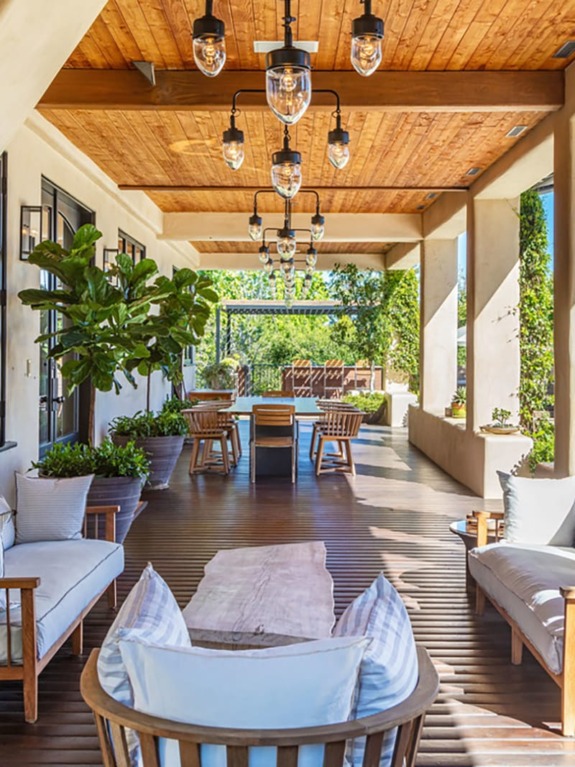 Spacious outdoor patio with wooden furniture, lush plants, and overhead lighting, perfect for relaxing and entertaining.