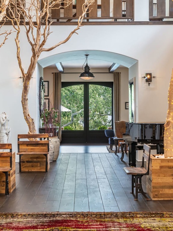 Modern living room with rustic wooden furniture, large windows, indoor tree, and piano, creating a cozy and natural ambiance.