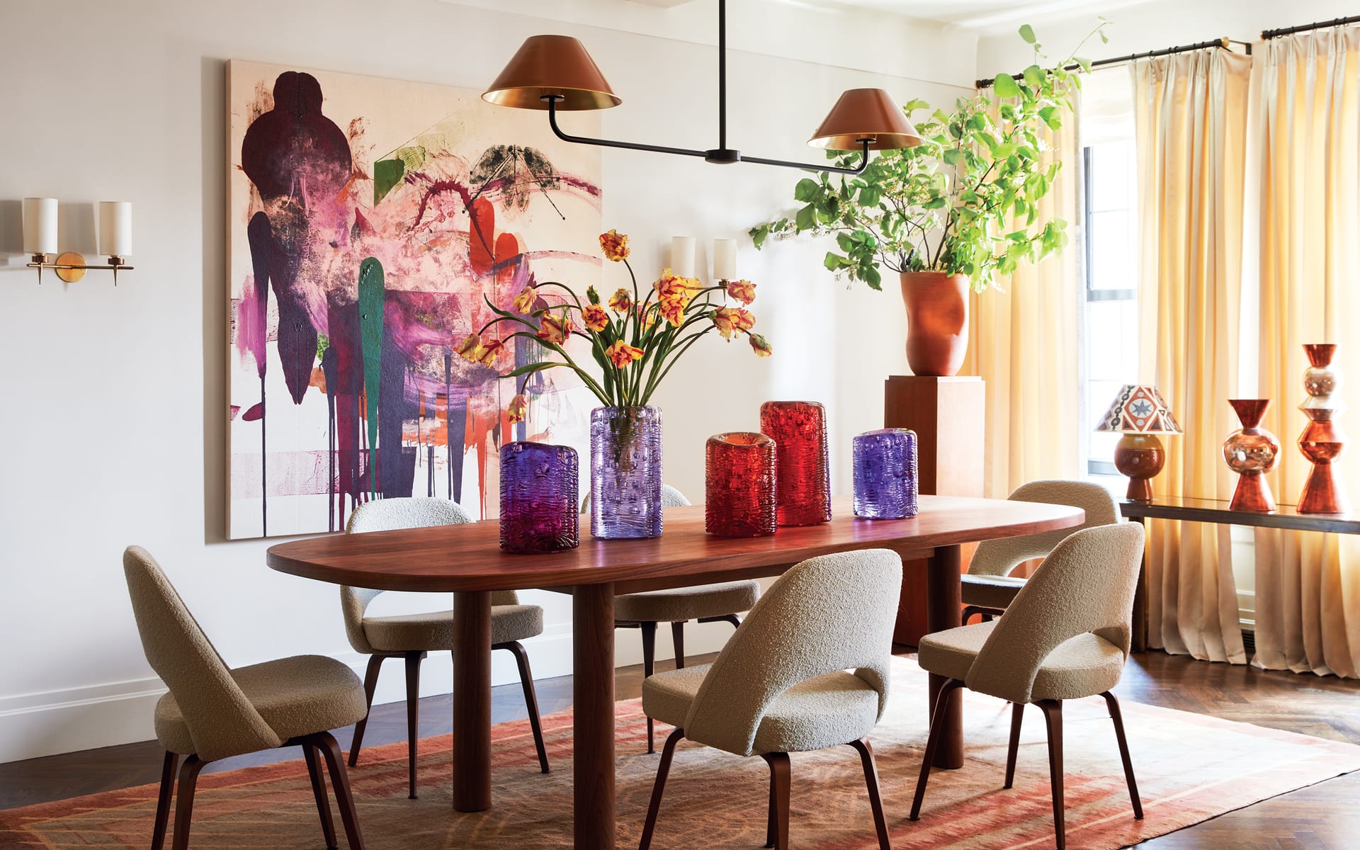 Modern dining room with abstract art, wooden table, contemporary chairs, colorful vases, and large window with beige curtains.