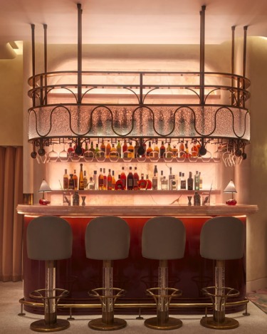 Elegant bar interior with stools, a variety of liquor bottles displayed, and warm ambient lighting.