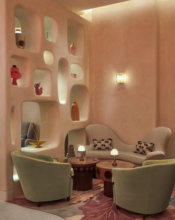 Cozy lounge with plush green chairs, abstract shelving, decorative vases, and soft lighting for a warm, inviting atmosphere.