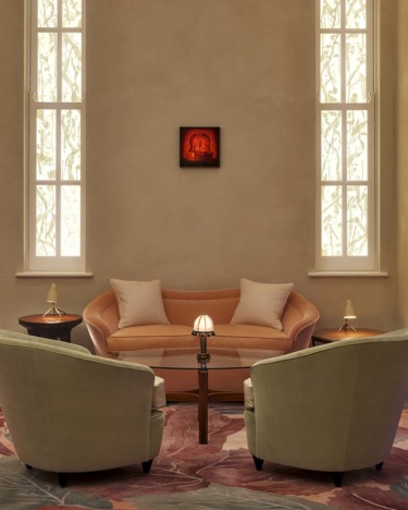 Elegant living room with a peach sofa, two green chairs, and a small table lamp under tall windows and warm lighting.