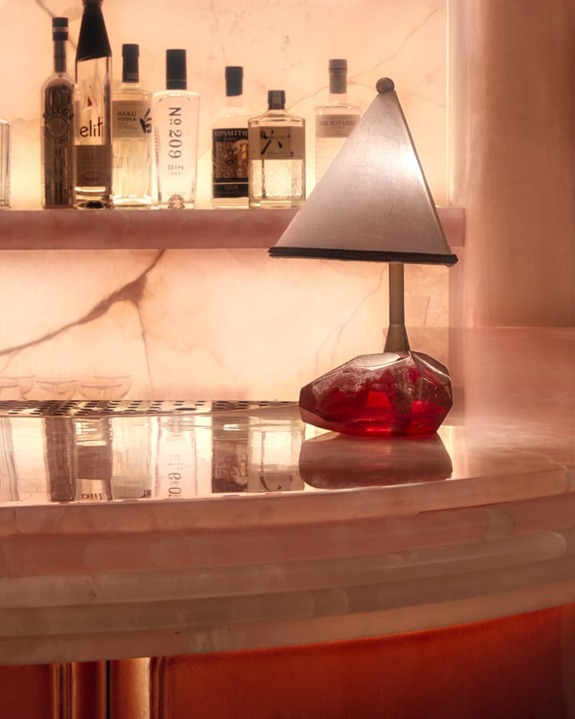 Elegant bar countertop with a red gemstone lamp and assorted liquor bottles on a backlit shelf.