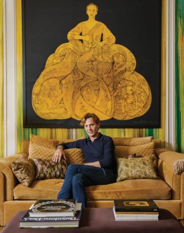 Person seated on a sofa with cushions, in a room featuring a large, intricate golden artwork on the wall behind.