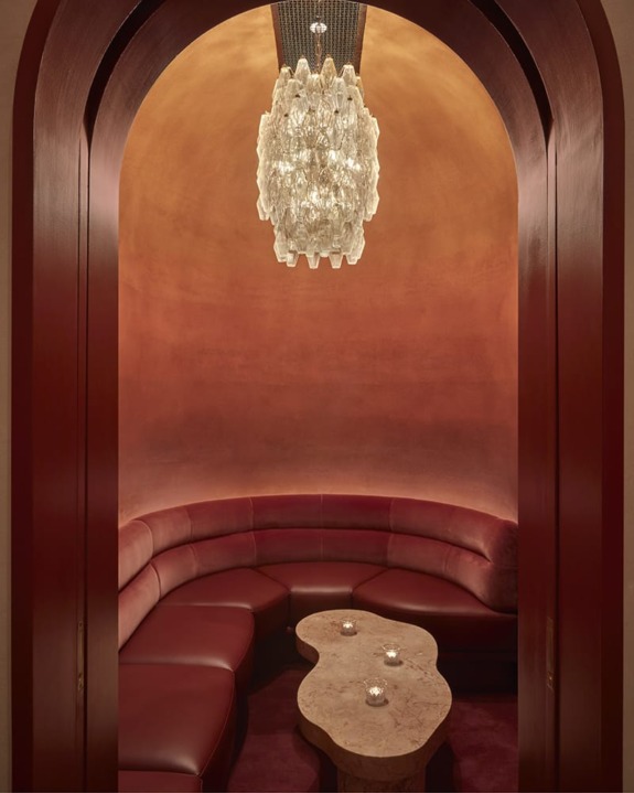 Luxurious curved seating with marble coffee table under an ornate chandelier in an elegantly designed room.