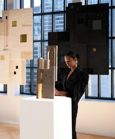 Woman in a gallery with contemporary sculptures and city view through large windows in the background