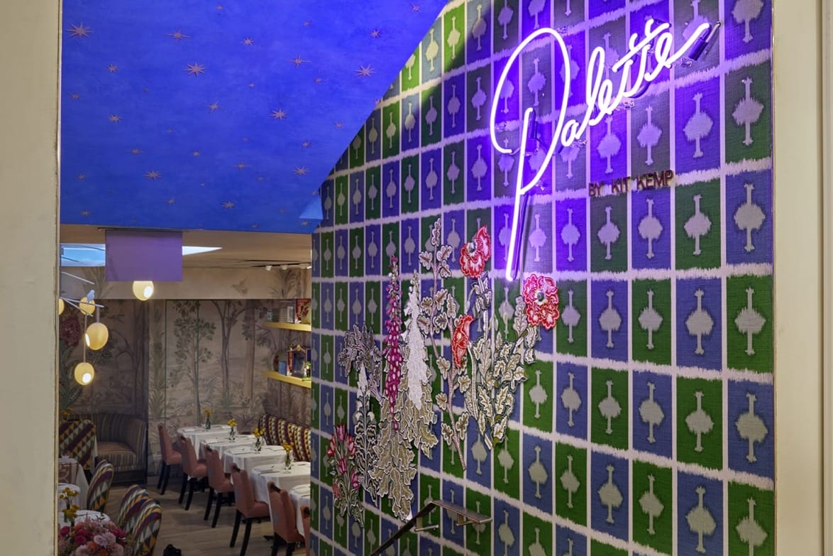 Colorful restaurant interior with patterned walls, neon sign reading "Palette", floral decor, and tables set for dining.