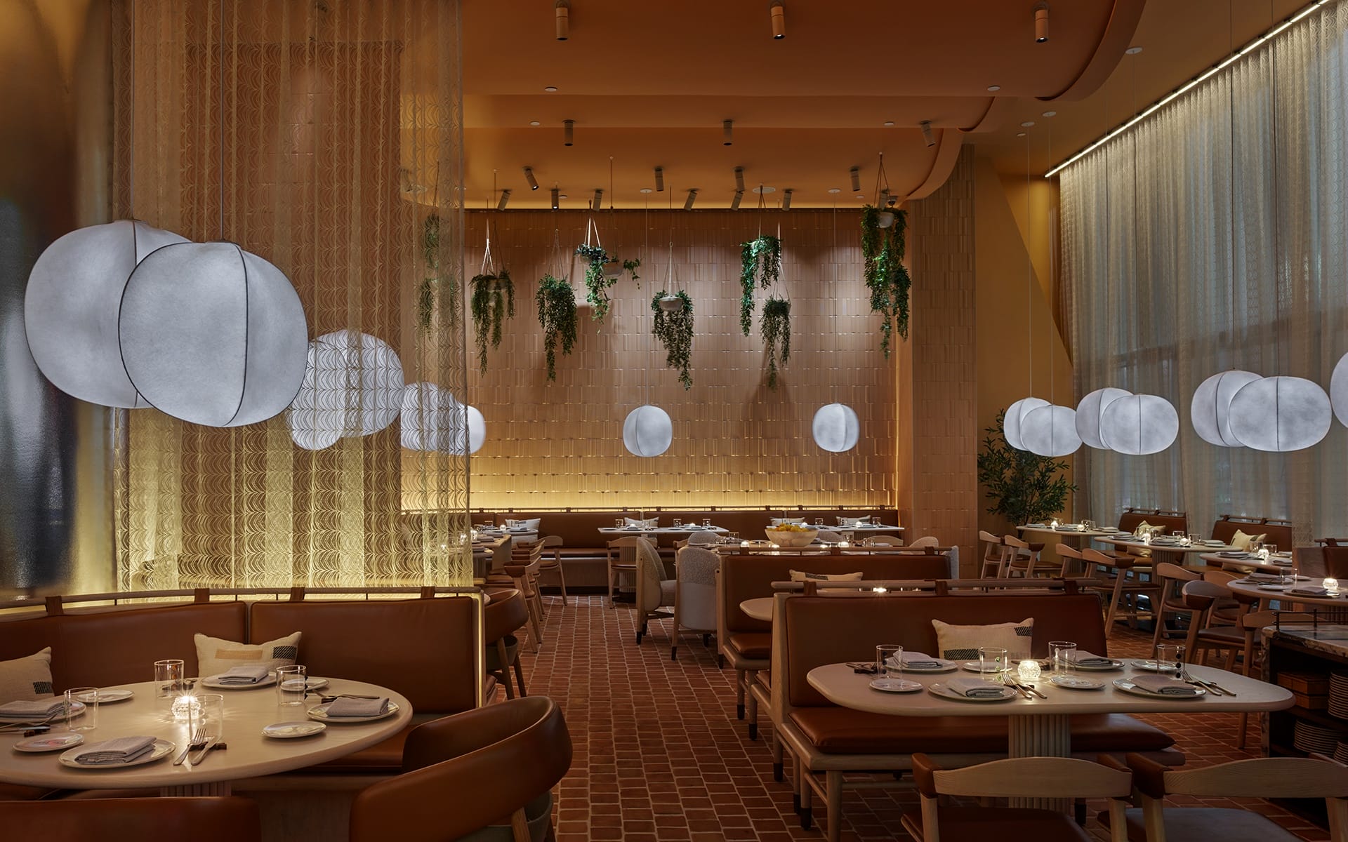 Modern restaurant interior with warm lighting, hanging plants, round pendant lights, and elegantly set dining tables.