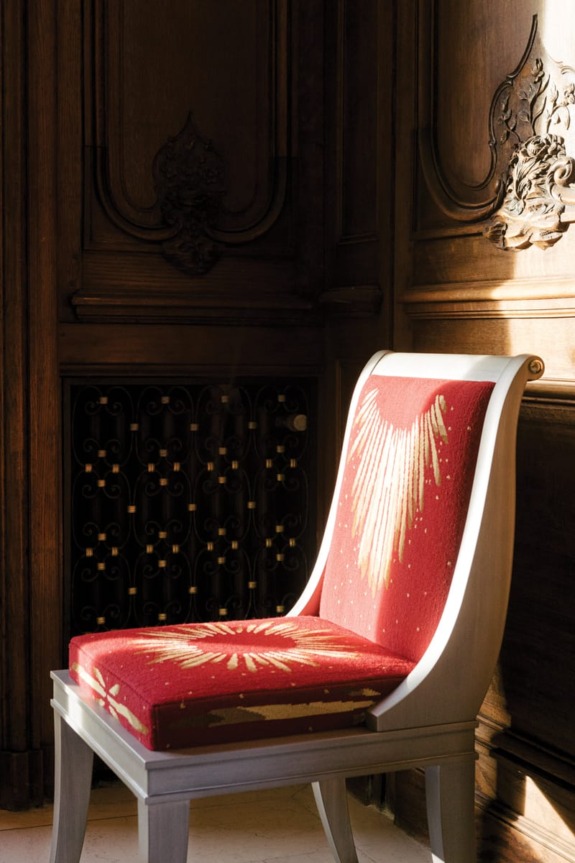 Elegant chair with red and gold patterned cushion in a room with ornate wooden paneling and soft natural light.