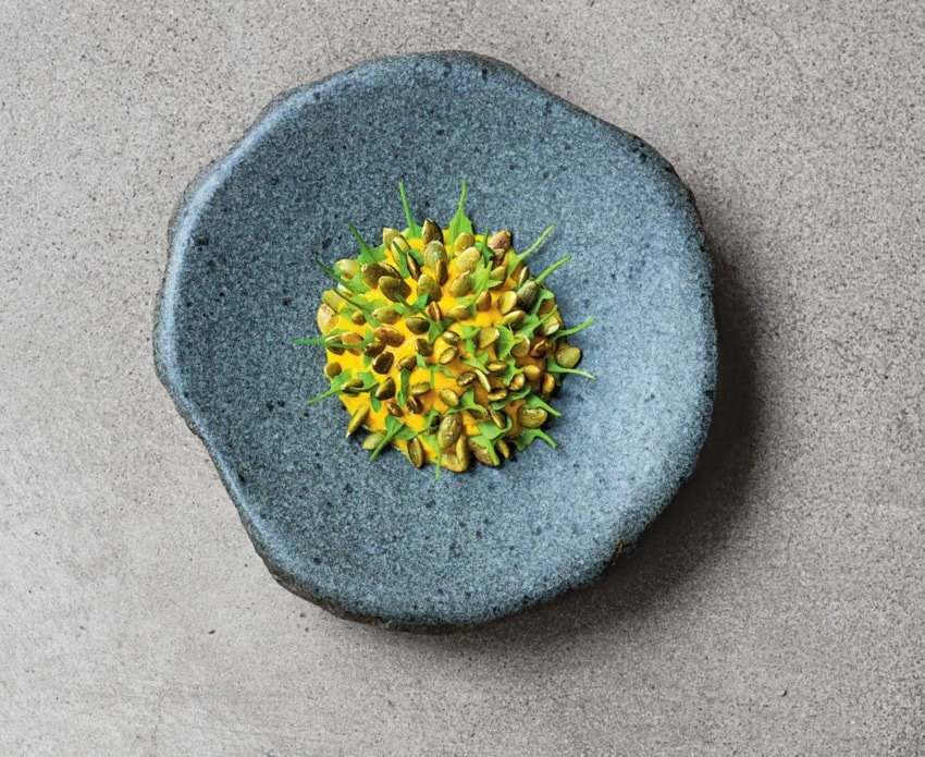 Plate with a gourmet dish artfully arranged on a textured blue surface against a gray background.